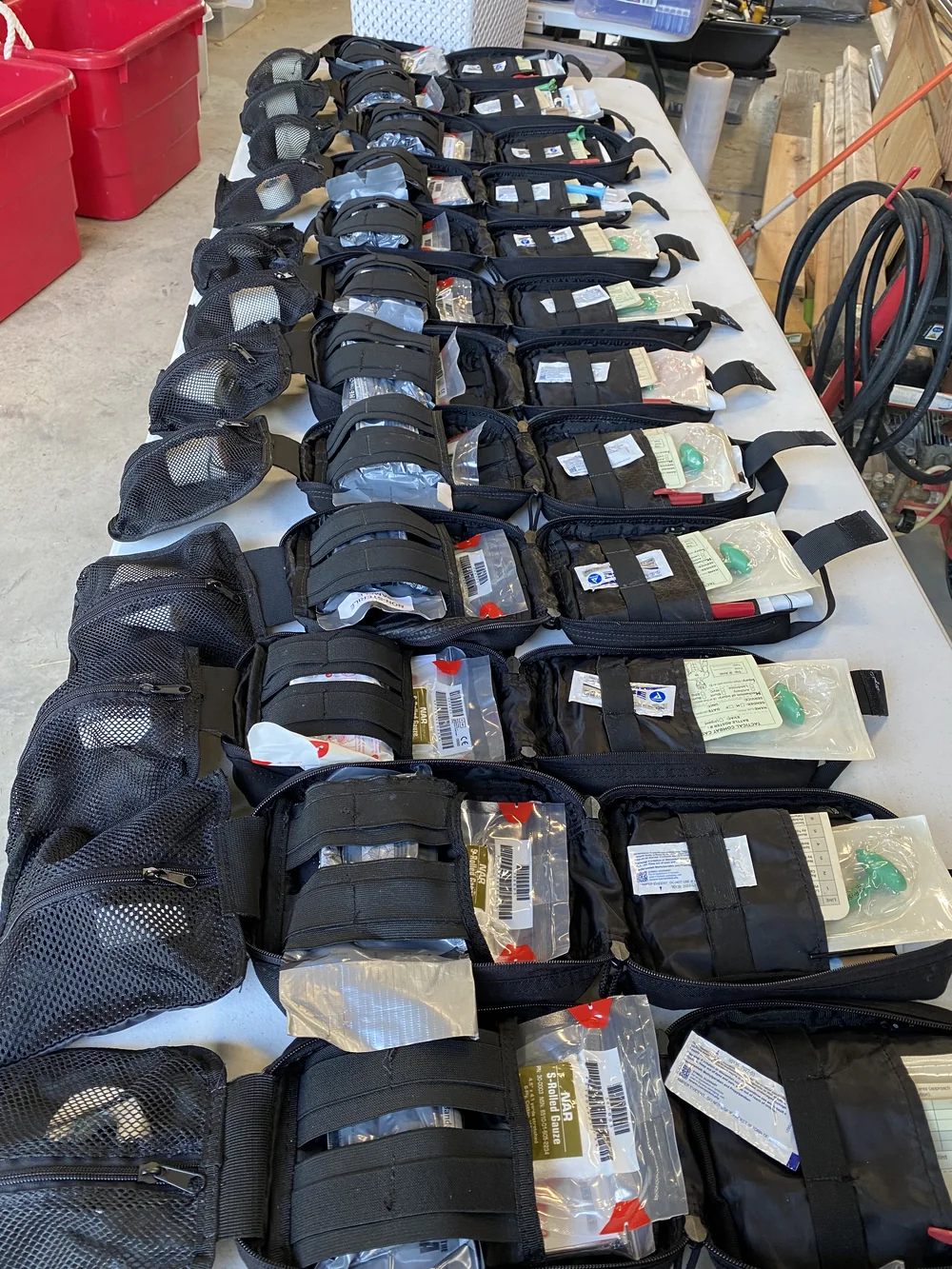 A long table covered with open individual first aid kits laid out in rows, each stocked with gauze and airway supplies.