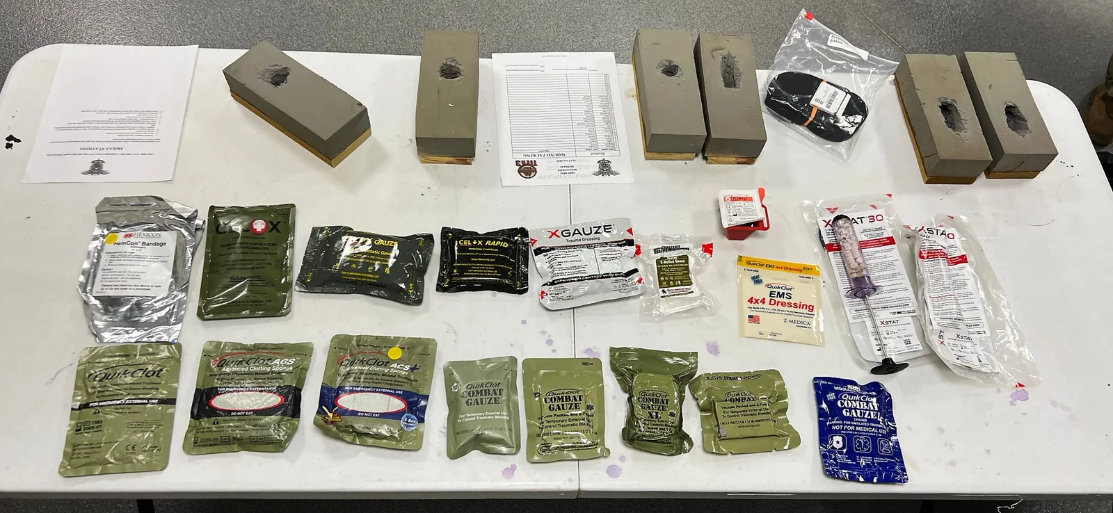 A skills station table with hemostatic gauze packages laid out beside ballistic wound-packing training blocks.
