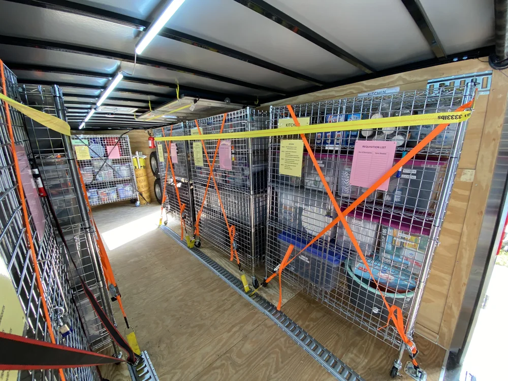 Wire supply cages inside a trailer, secured with orange and yellow ratchet straps.
