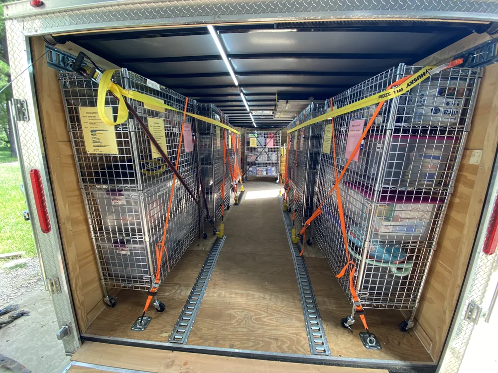 Interior of a mobile training trailer with rolling wire supply cages secured by ratchet straps.
